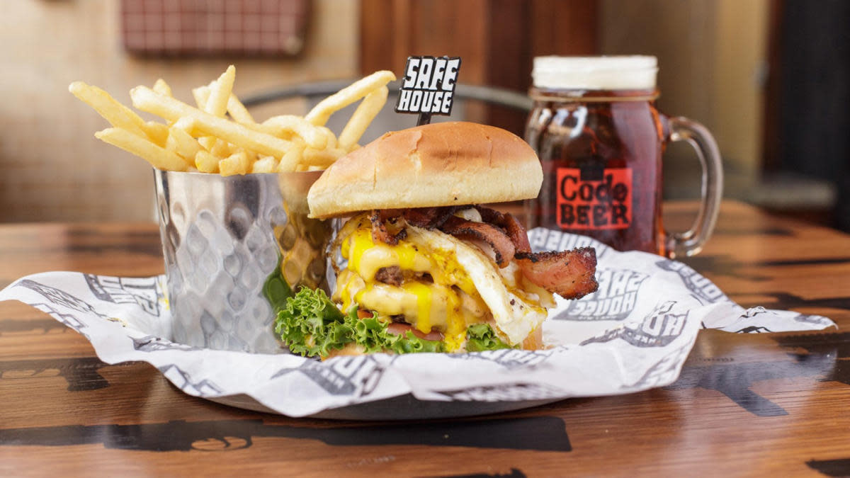 Burger topped with bacon, cheese and a fried egg, served with french fries and a mug of root beer at SafeHouse Milwaukee.