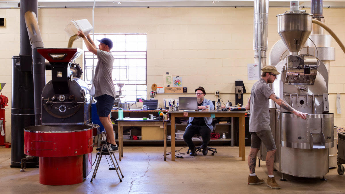 Anodyne Coffee employees work beside large commercial coffee roasters inside the Milwaukee roastery.