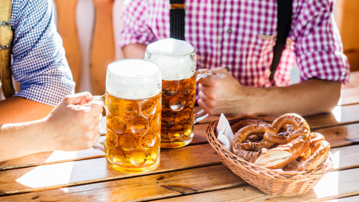 Two steins of beer and a side of pretzels in front of two men in lederhosen