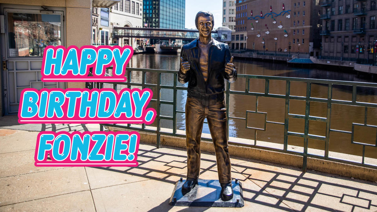 Statue of the character Fonzie giving a thumbs-up along the Milwaukee Riverwalk, with colorful text that reads “Happy Birthday, Fonzie!” overlaid on the image.