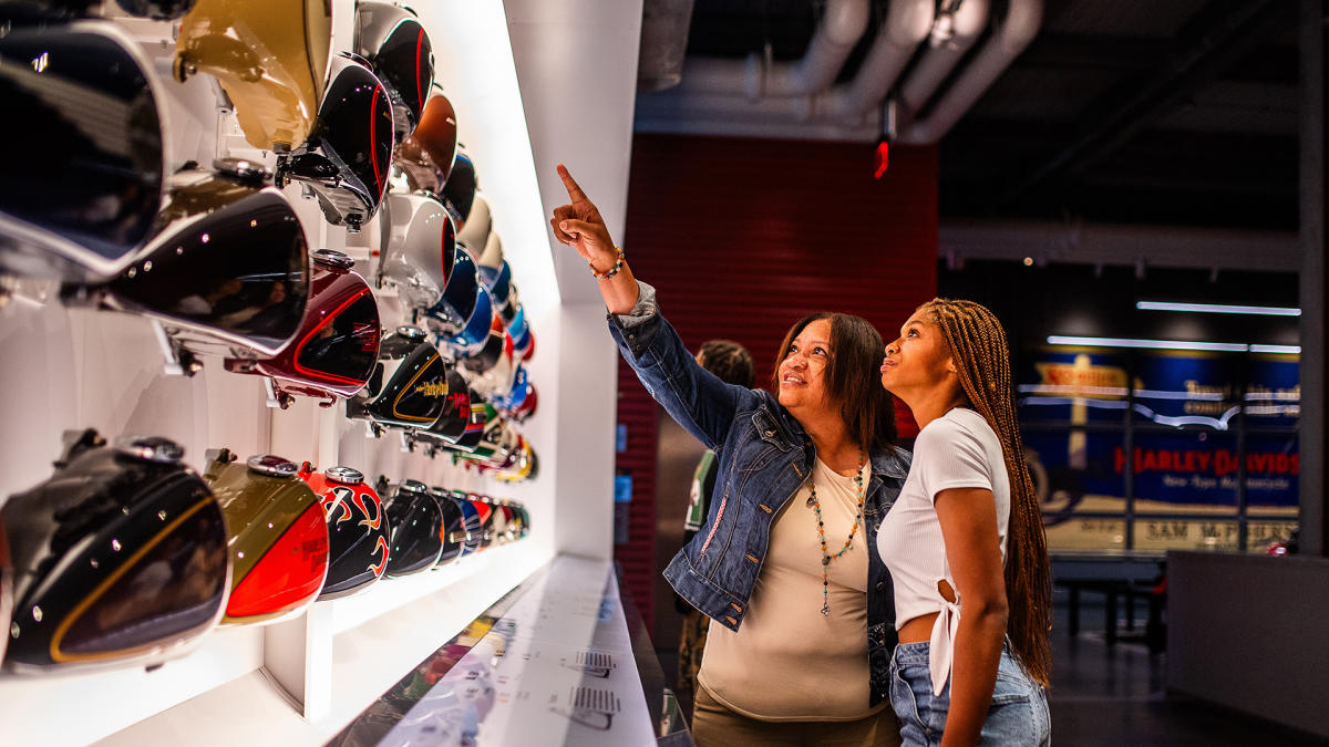 a mother and daughter pointing at a wall of motorcycle tanks