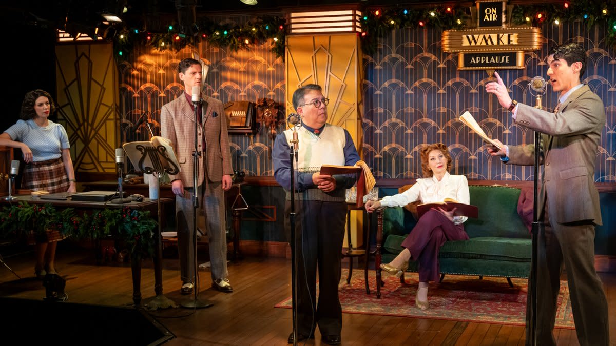 Actors perform a live radio play on stage styled like a 1940s broadcast studio, complete with vintage microphones, scripts in hand, and art deco decor. One performer stands at a microphone delivering lines while others look on, creating the feel of an old-time radio drama.