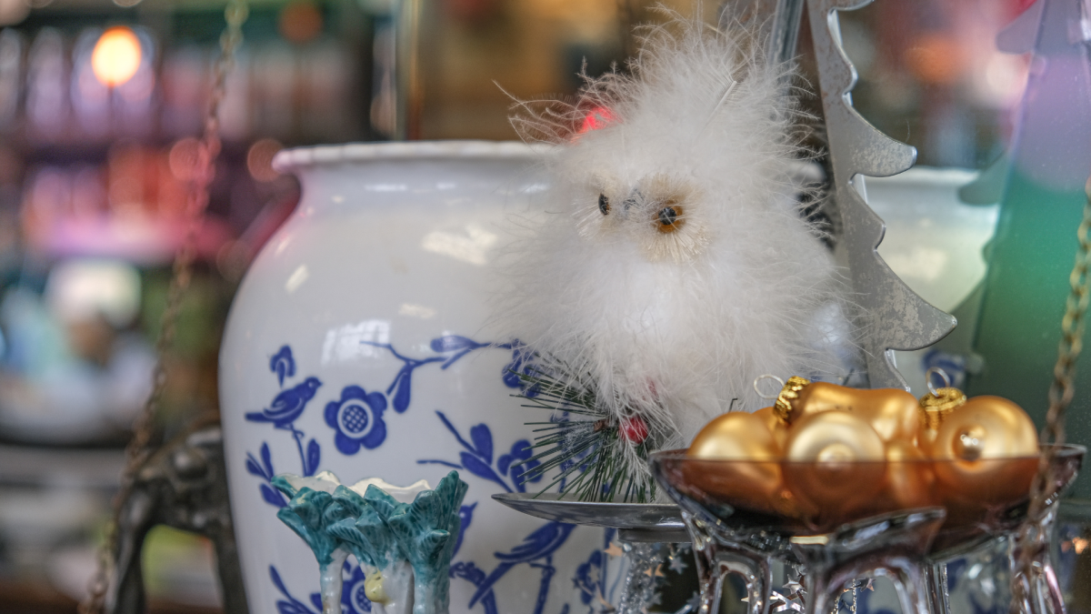 A decorative display featuring a white fluffy owl perched on a blue and white porcelain vase, accompanied by a silver tray holding golden ornaments.