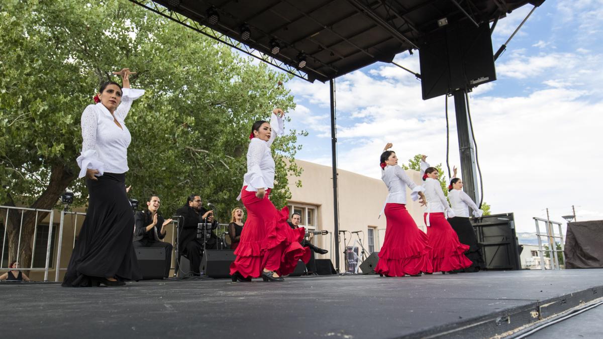 Five people in white shirts and red flamenco dresses perform on an outdoor stage