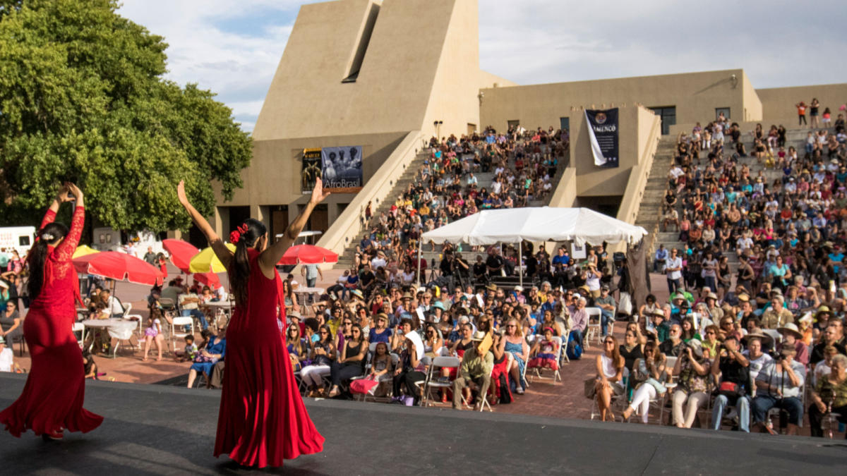 Two performers in red flamenco dresses gesture before a large crowd