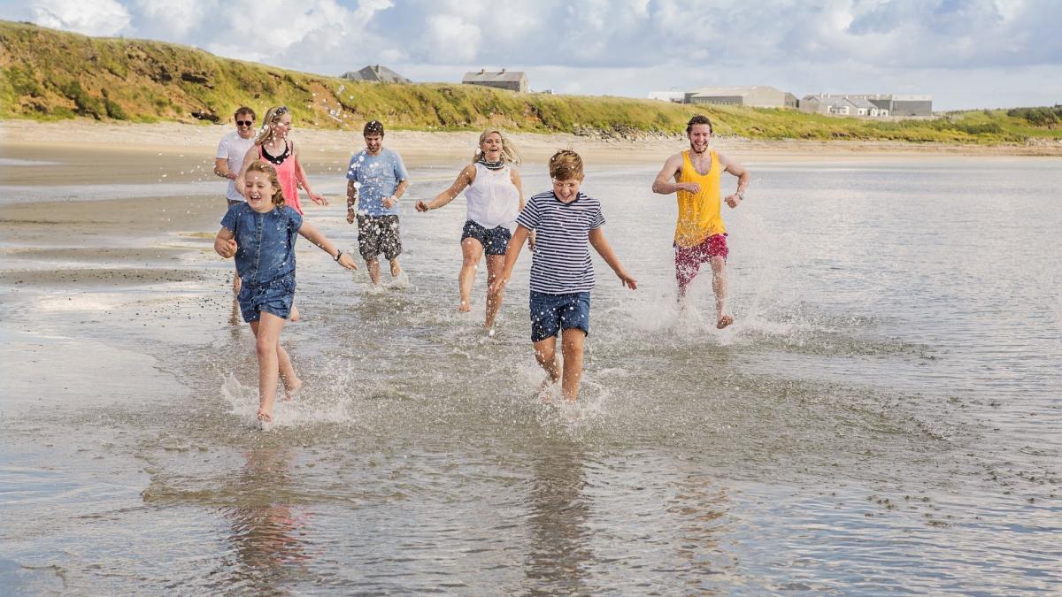 Family enjoying a day out at Ballyhornan Beach, County Down, splashing in the waves