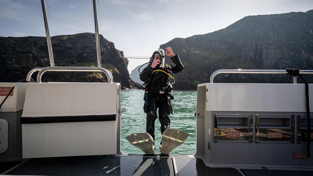 Scuba diver falling backwards from a boat while giving a thumbs up