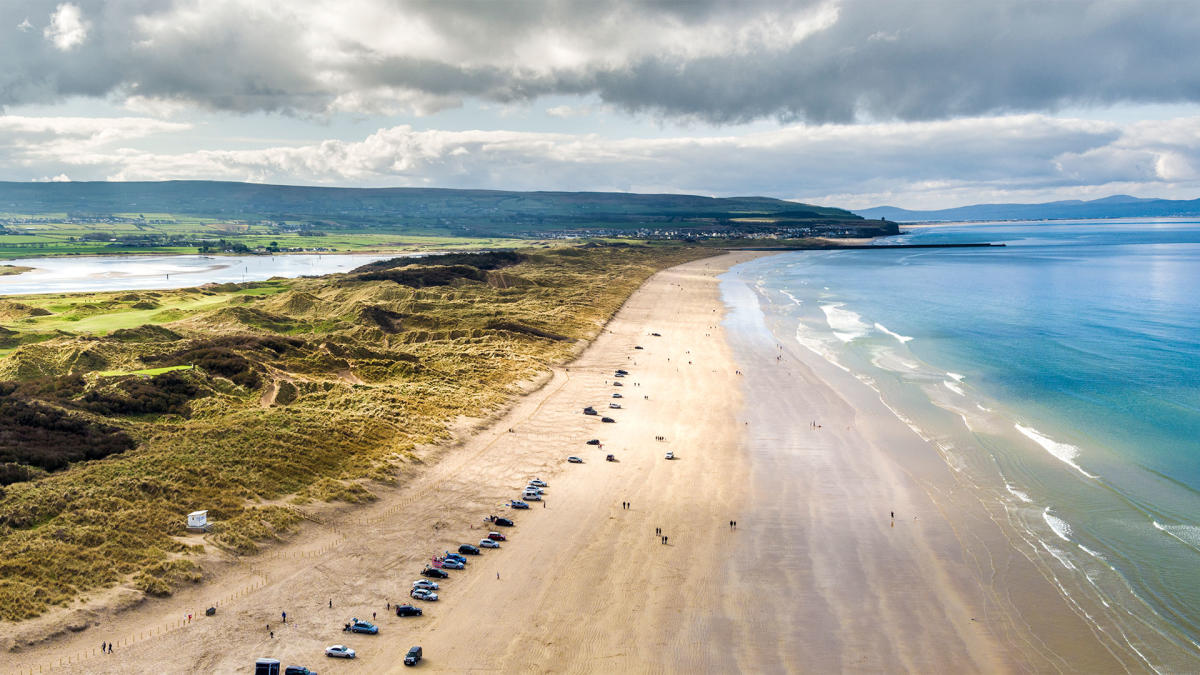 Aerial view of Portstewart beach with cars parked along the stretch of sand.