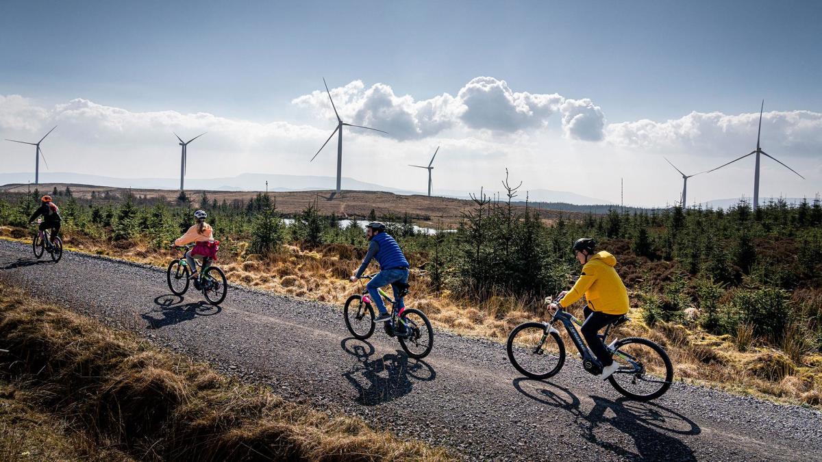 Group in single file on electric bikes with wind turbines in the background, enjoying the Electric Escape experience with Corralea Adventure