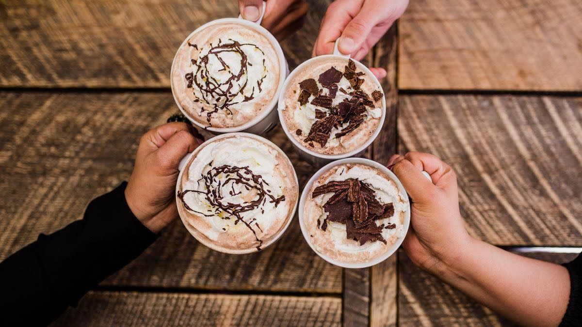 Looking down at 4 hands toasting gourmet hot chocolate mugs