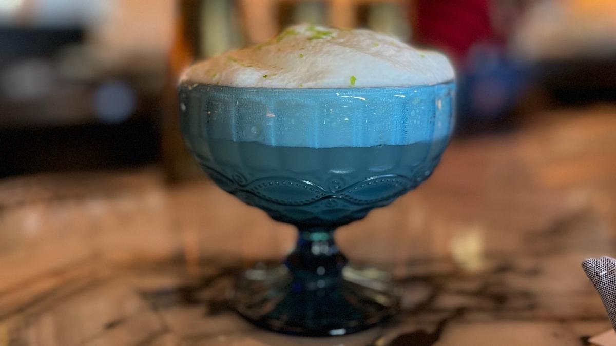A cocktail called The Brock sits on the counter in a blue glass at Bar Cecil in Palm Springs.