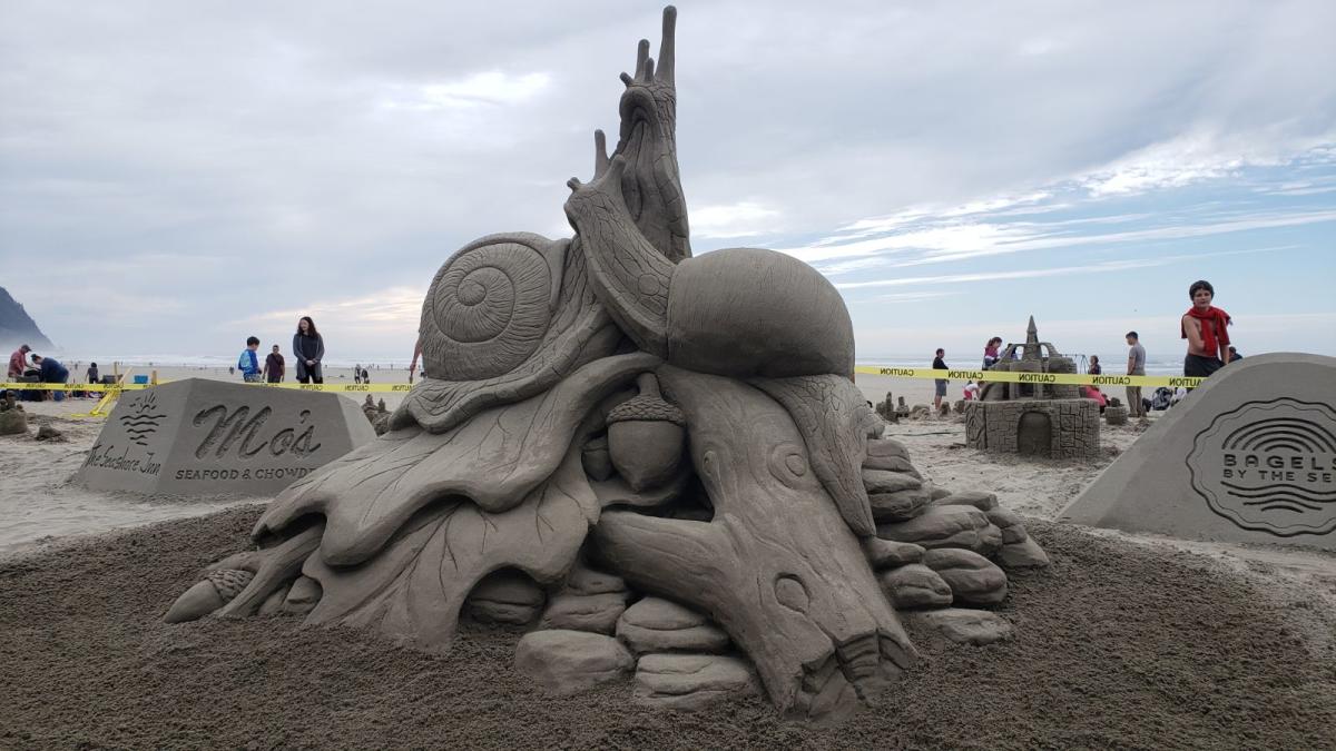 Sand sculpture of a couple of slugs wrapped around part of a tree. A couple of leaves and acorns are visible around.