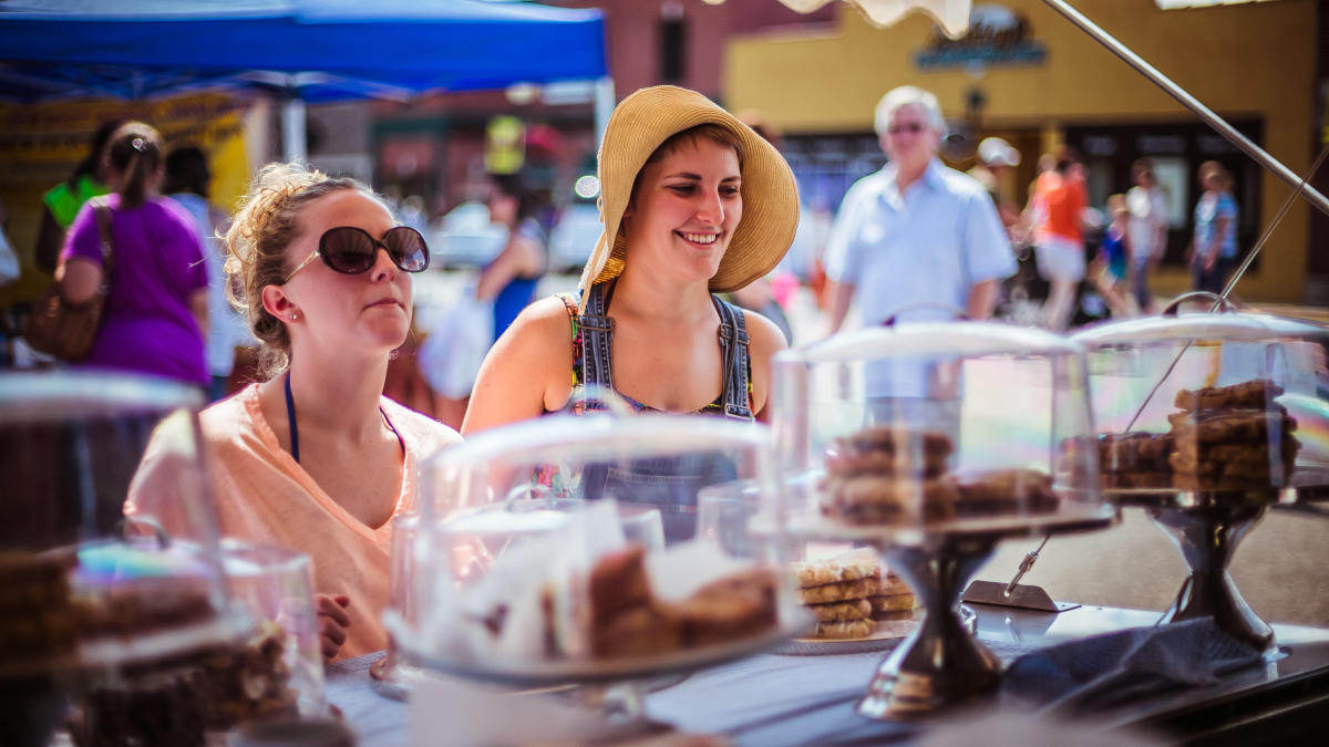 Two women look at baked goods under glass domes.