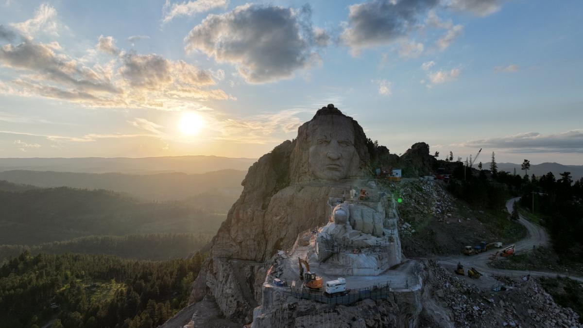 looking straight on at Crazy Horse memorial with the sun setting and black hills behind the statue