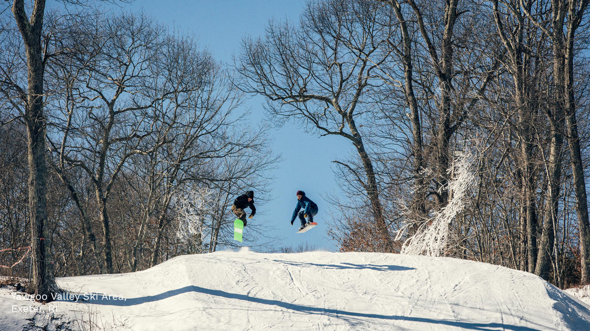 Two snow boarders coming up over a hill
