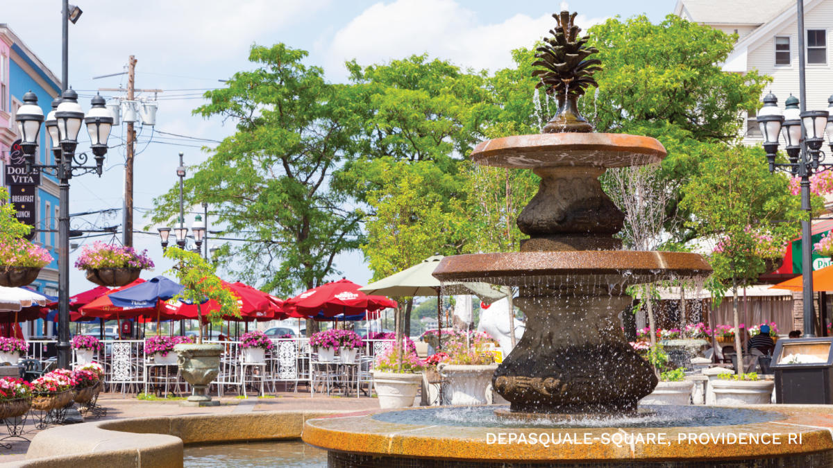 The fountain in Depasquale Plaza surrounded by outdoor dining tables and bright red umbrellas.