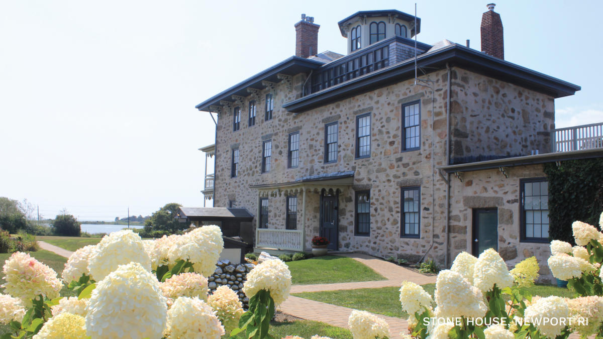 A tan and brown stone building with a green lawn and cream hydrangeas in front.
