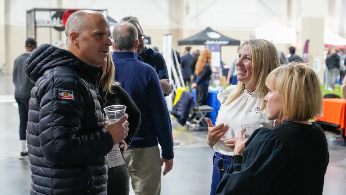 3 smiling people socializing with sports activities and booths in the background
