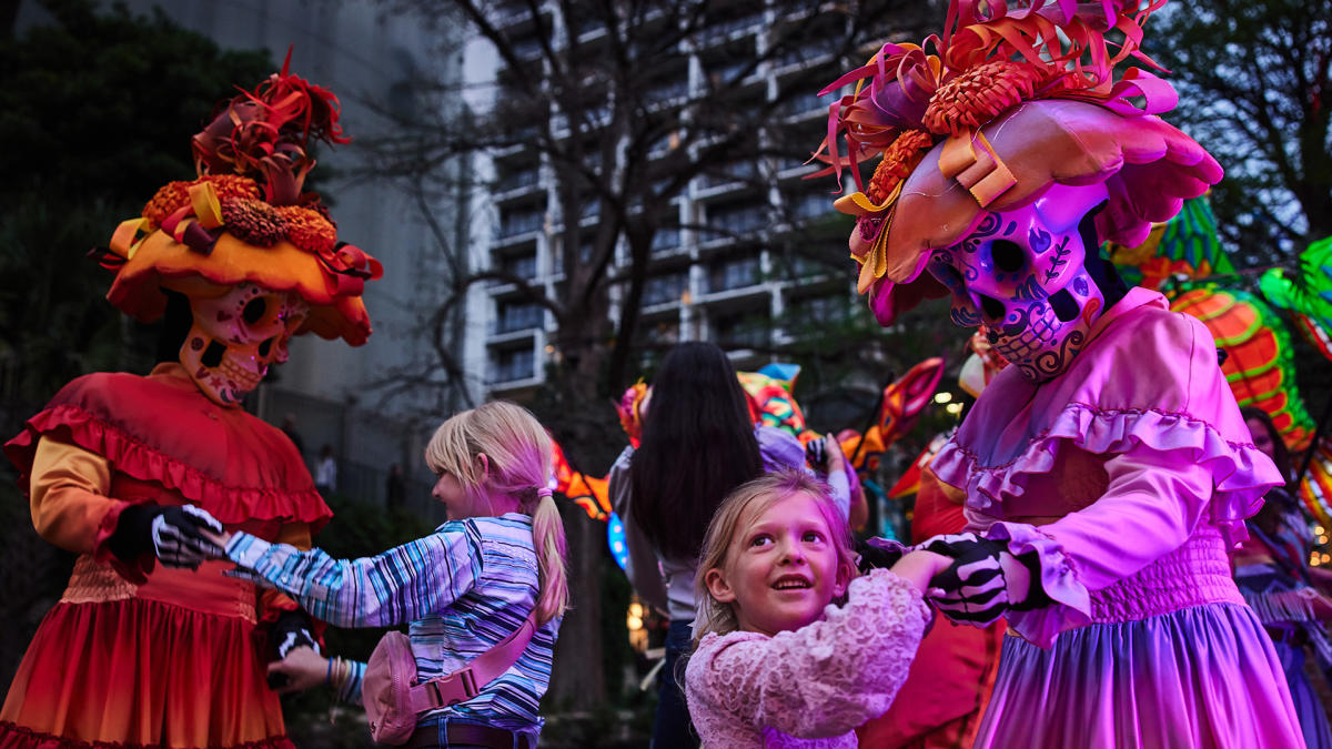 Two children dancing with costumed dancers in Day of the Dead attire
