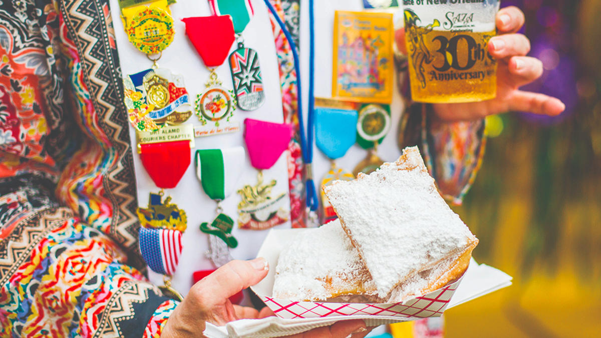 Person holding pastries in powdered sugar wearing Fiesta medals