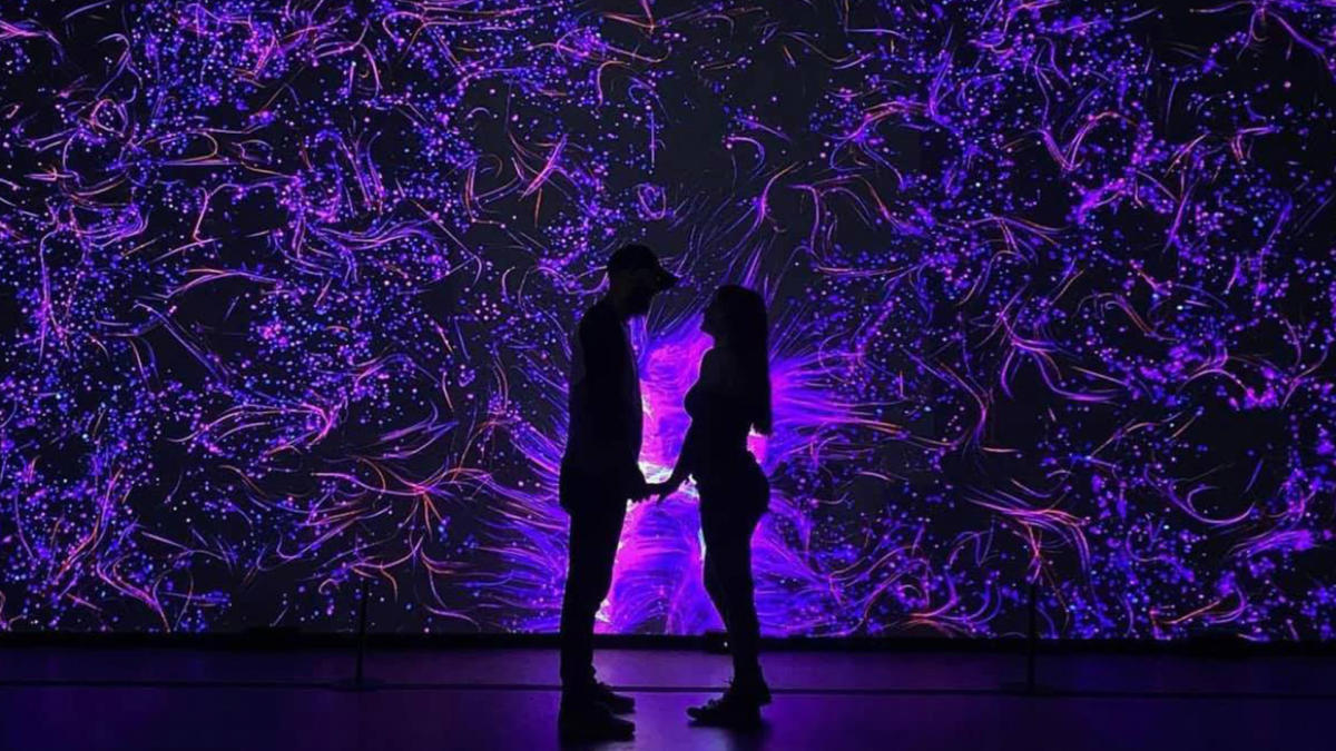 Couple holding hands in front of illuminated art installation