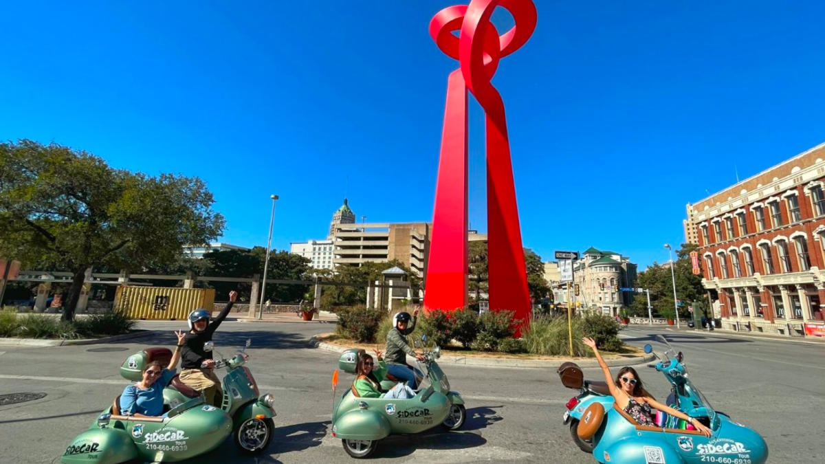 Three sidecar tours driving in front of San Antonio's Torch of Friendship sculpture