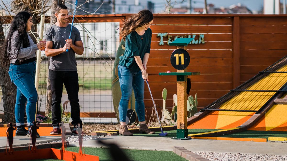 Three people playing putt-putt golf at a bar