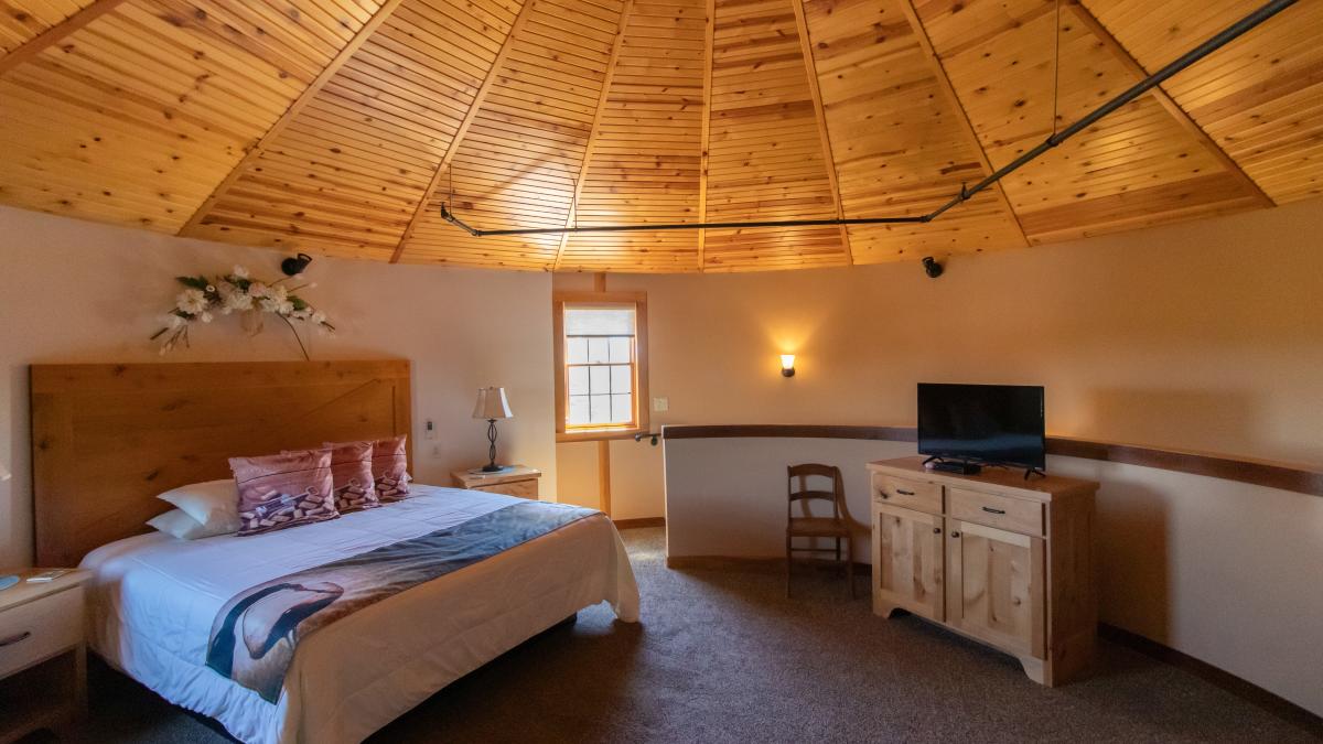 Cozy, round hotel room with a wood-paneled ceiling, king bed, and rustic furniture.