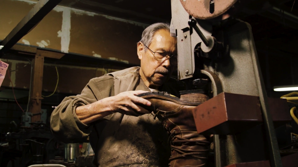 Older man sitting at an industrial machine crafting a leather cowboy boot