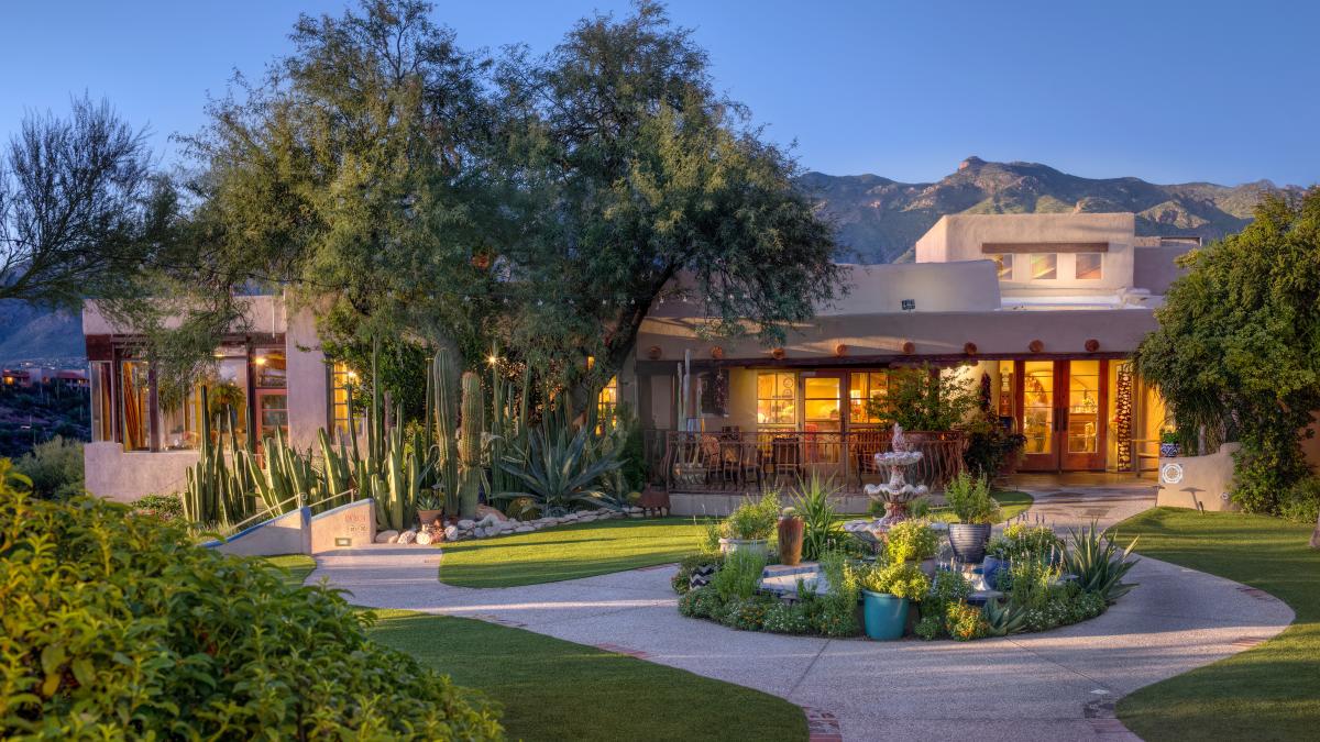 exterior of a brown southwest-style building with cacti, desert plants, and other greenery surrounding it