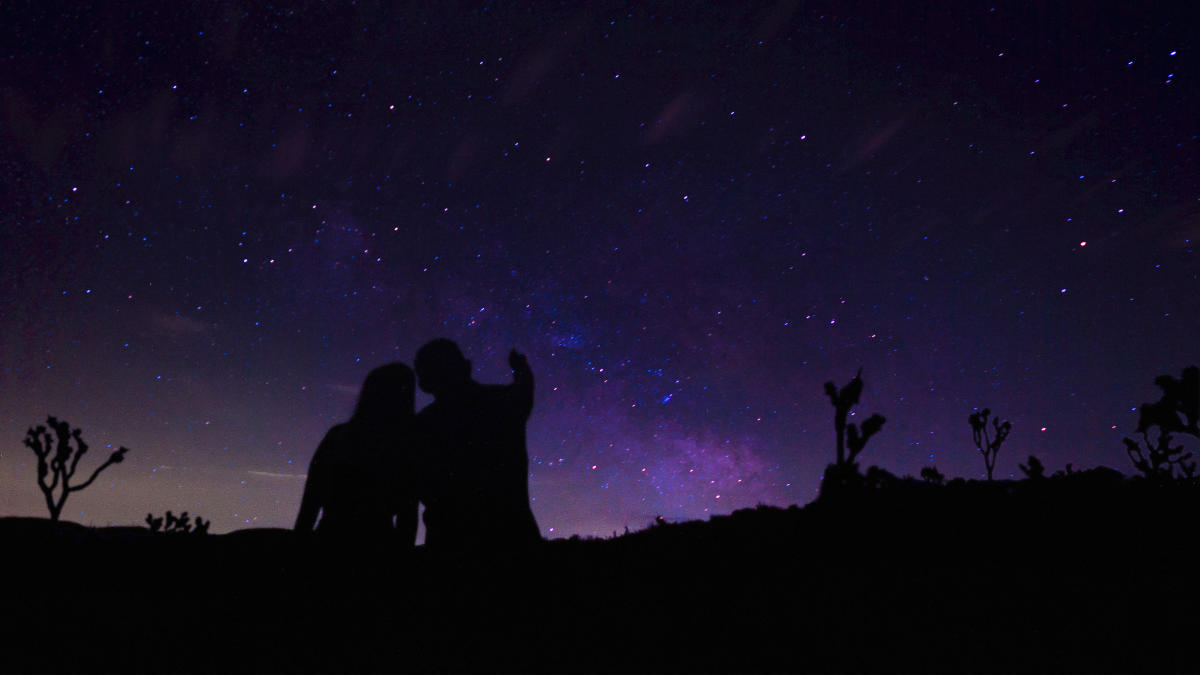 A couple standing together pointing to the stars in Joshua Tree National Park, just outside Twentynine Palms, California.