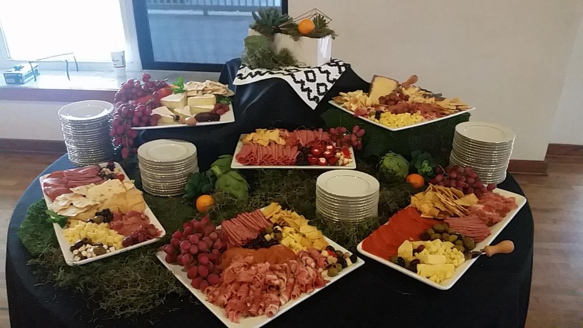 A table full of sliced meats and cheeses, fruit, and other finger foods is displayed at a catered event