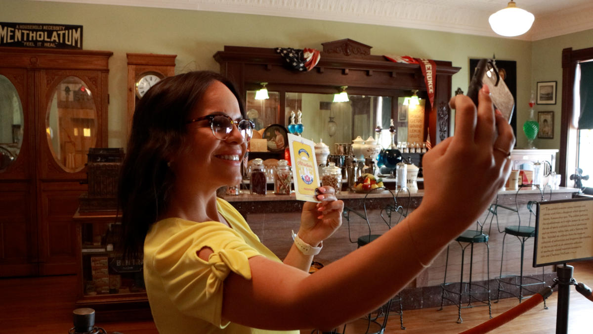 A young woman takes a selfie with the Wichita Attractions Tour passport in her hand