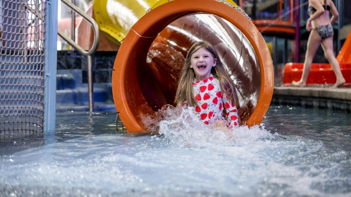 A young girl smiles as she exits the end of a tube water slide at Blast Off Bay