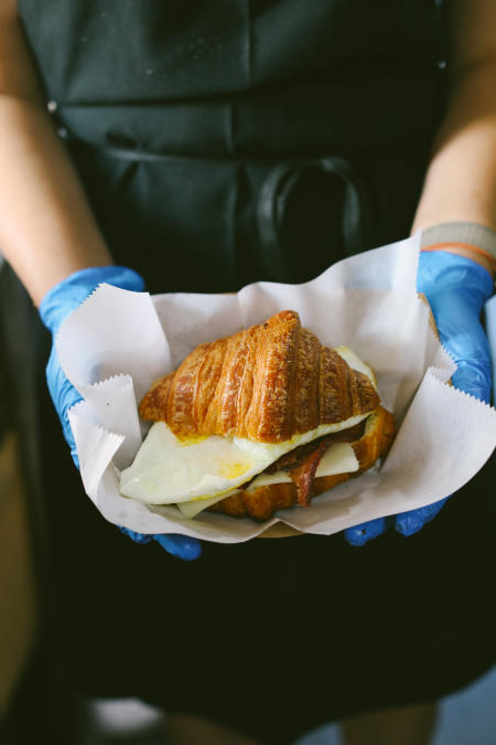 a man holding a fresh croissant egg and bacon sandwich