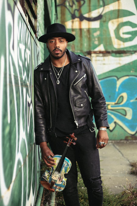 Damien Escobar stand in front of a grafitti wall holding a violin