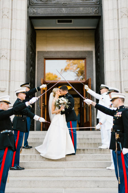 A couple kisses on the steps of the US Naval Academy Chapel with military salute.
