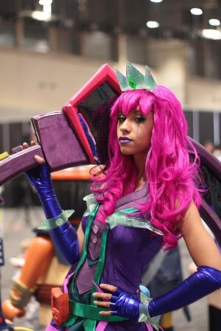 A woman wearing pink wig and holding a giant foam axe is ready for cos play