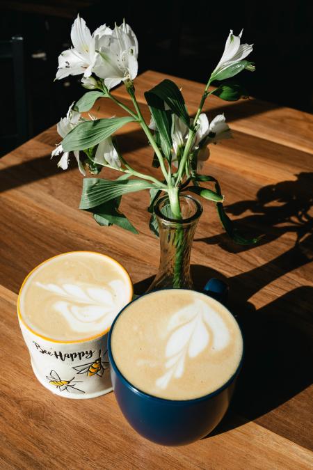 Two cups of coffee and a vase of white flowers arranged on a table.