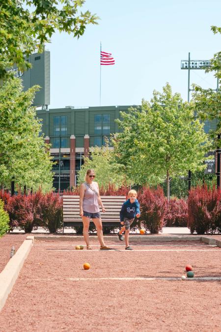 Mom and young son playing Bocce ball at Titletown with the Lambeau Field behind them.