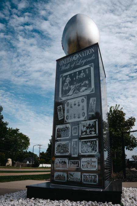Marble statue with a large silver steel football on top of the marble pillar and Oneida Nation Walk of Legends information engraved.