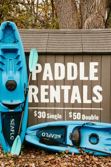 Paddle Boards lying against a shed with the writing "Paddle Rentals: $30 Single and $50 Double"