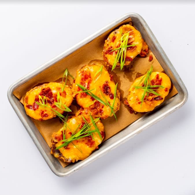 The image is of a metal tray that contains potato skins covered in cheese, bacon and chives.