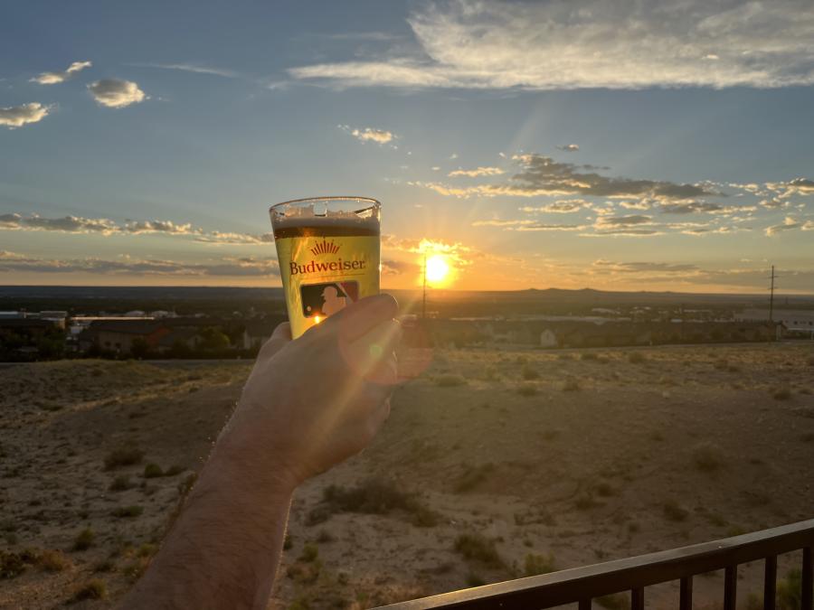 Someone holds a glass of beer up as the sun is setting at The Landing with Pizza 9.