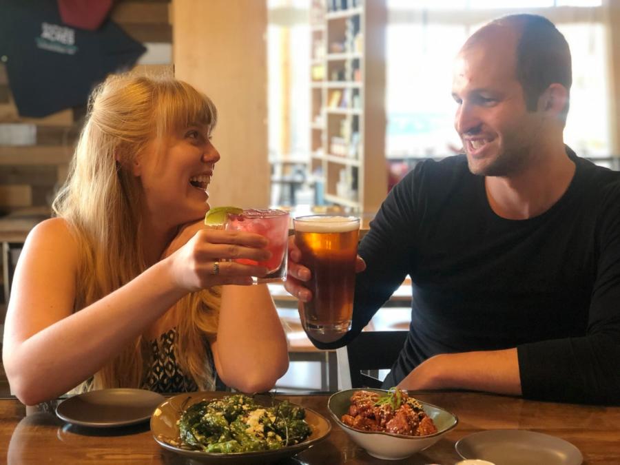 A man and woman cheers above two plates of food from Sixty Six Acres