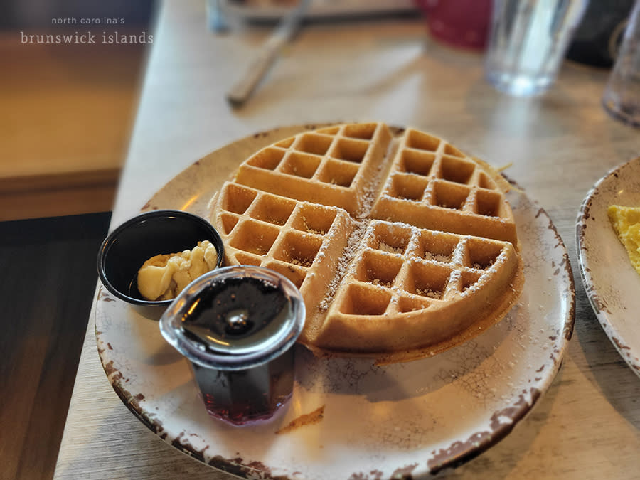 a Belgian waffle on a plate with a side of syrup and butter
