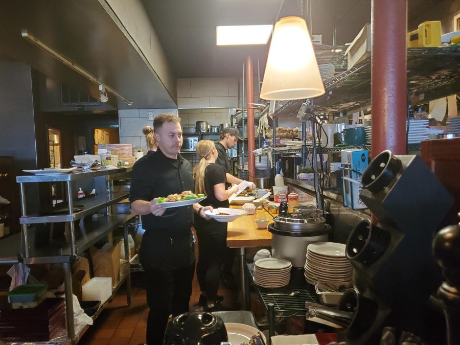 A busy kitchen scene with a server holding plates ready to go out to the tables