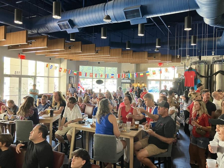 A group of people gathered in a casual restaurant facing TV screens to watch a ball game