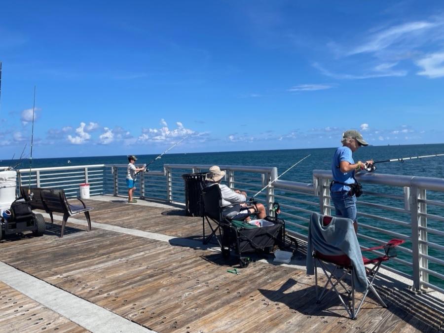 A child, an older gentleman in a chair, and a middle-aged man fishing from a pier.