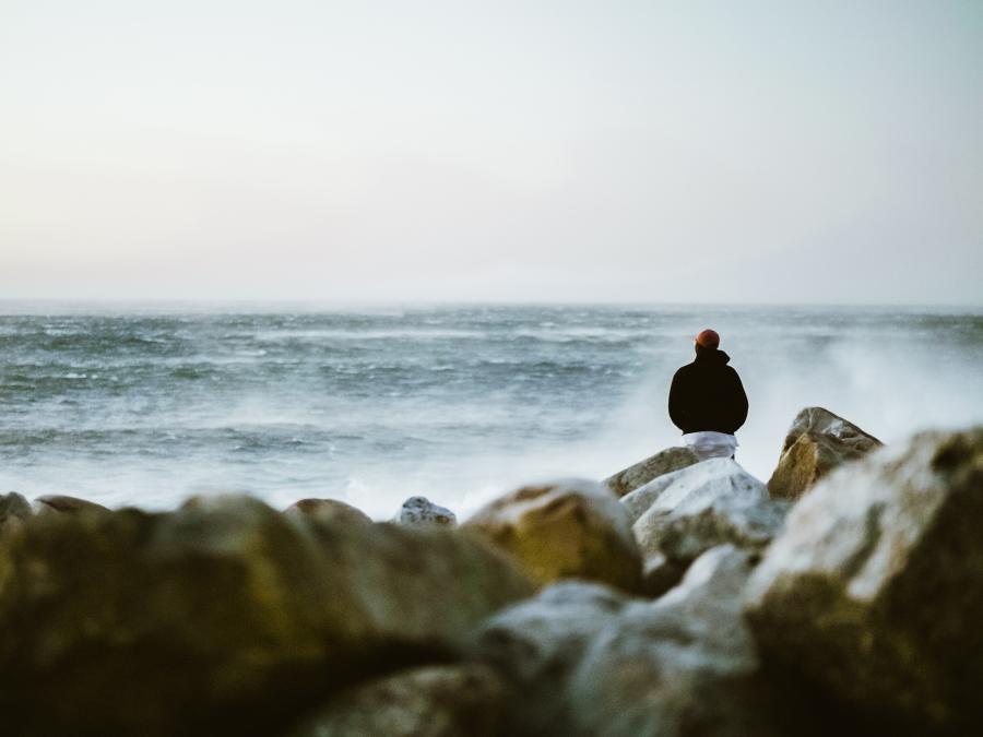 Man sitting on rocks looking at the crashing waves in Half Moon Bay